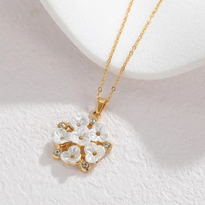 Elegant 18k gold floral necklace with white shell flowers and crystal centers on a stone base