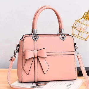 Detail of pink bow handbag featuring heart-shaped metal link and premium leather texture