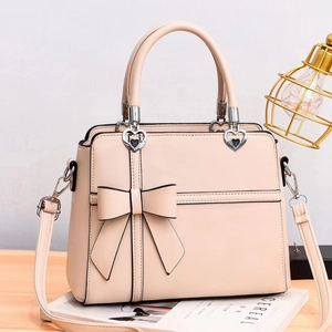 Pale pink leather handbag with large bow detail and heart-shaped metal hardware on wooden desk