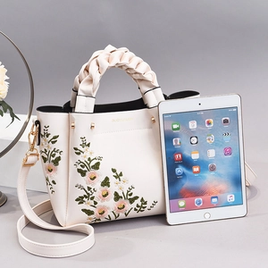 White faux leather handbag with floral embroidery and woven handle next to a tablet