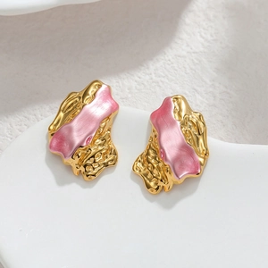 Irregular textured gold and pink earrings on a decorative white ceramic tray