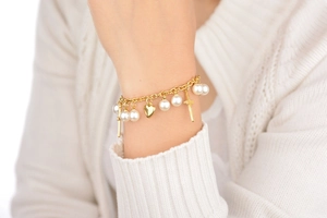 Gros plan d'un bracelet doré avec perles, cœur et croix portés sur un poignet délicat