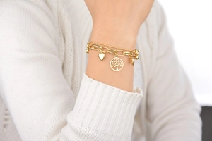 Gros plan d'un bracelet double couche doré avec breloques arbre de vie et cœur sur le poignet
