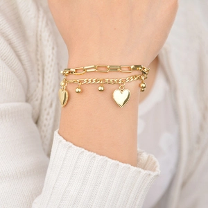 Détail d'un bracelet doré à plusieurs rangs avec breloques cœur porté par un mannequin