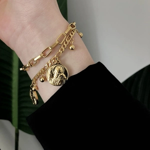 Détail de bracelets dorés superposés avec médaille religieuse et pendentifs perlés