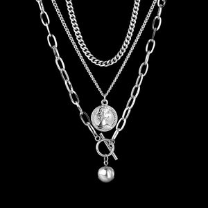 Close-up of silver layered necklace with portrait coin, metal ball, and toggle clasp