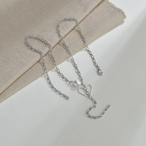 Detail of silver double-layered chain necklace with heart pendant and pearl on linen fabric