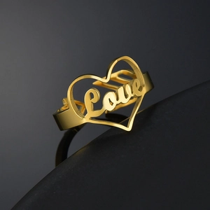 Detail of golden heart-shaped open ring featuring cursive Love engraving on metal