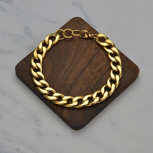 Close-up of polished gold Cuban link chain bracelet with lobster clasp on wood stand