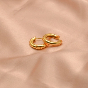 Nahaufnahme goldener Creolen mit poliertem Finish auf weichem rosa Seidenhintergrund