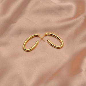 Detail of glossy gold oval hoop earrings on soft pink silk background
