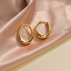 Detailed view of gold oval hoop earrings on soft purple silk fabric background