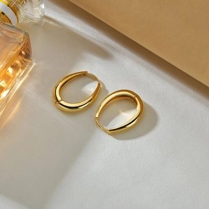 Polished gold oval hoop earrings displayed on a minimalist textured jewelry stand