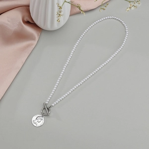 Collier de perles vintage avec fermoir OT et pendentif pièce reine sur fond gris clair
