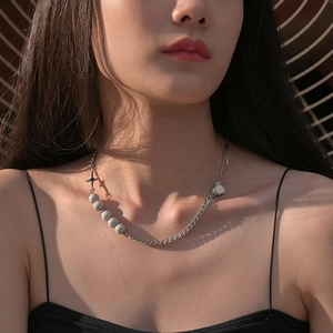 Asymmetric metal necklace with gray beads and cross pendant worn by a model