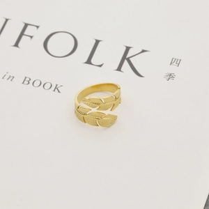 Gold leaf feather wrap open ring in minimalist stainless steel shown on white book