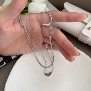 Détail d'un collier argenté à double épaisseur avec pendentif cœur et breloque Love