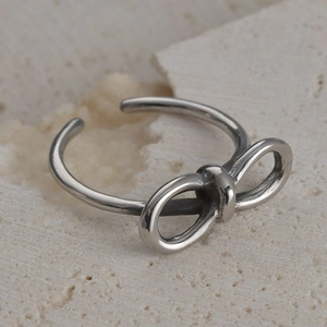 Close-up of a silver bow-shaped vintage steel ring on a textured beige stone background