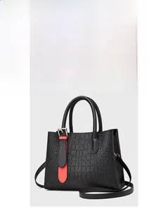 Close-up of black crocodile embossed leather handbag with contrasting red buckle strap