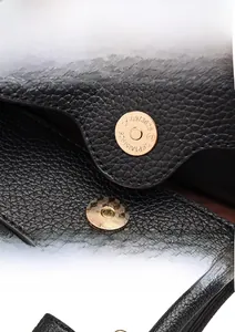 Close-up of golden magnetic snap closure and black lychee grain leather on handbag