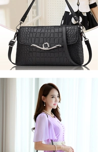 Detail of black crocodile embossed shoulder bag with round silver metal lock and strap