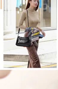 Detail of black faux leather crossbody bag with silver zipper and decorative scarf