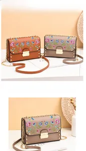 Close-up of floral embroidery on PU leather flap bags with gold rivets and chain strap