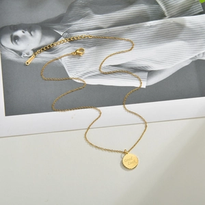 Minimalist gold stainless steel necklace with 'Good Luck' round pendant on a magazine