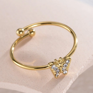 Adjustable golden butterfly ring with sparkling crystals on a pink marble background