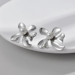 Artistic silver flower earrings with pearl accent displayed on a white textured plate