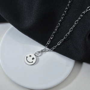 Détail du pendentif smiley à œil étoilé sur chaîne argentée avec contrastes noir et blanc