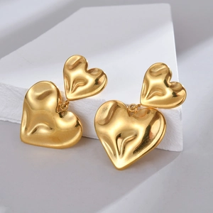 Detailed view of gold double heart earrings with hammered texture on white stone