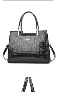 Detail of black faux crocodile leather handbag with golden logo and detachable shoulder strap