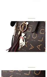 Close-up of golden cat pendant with red bow and leather tassel on brown patterned handbag