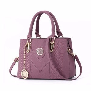 Close-up of lilac pebbled leather handbag with gold metal logo and chain pendant