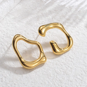 Irregular geometric gold earrings on white stone background with soft feather accent