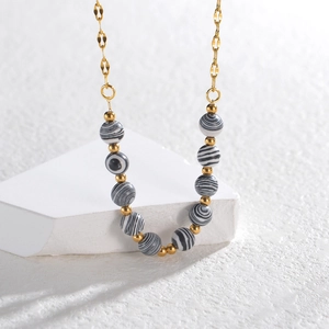 Chic gold necklace featuring black and white striped beads and gold spacers on white stand