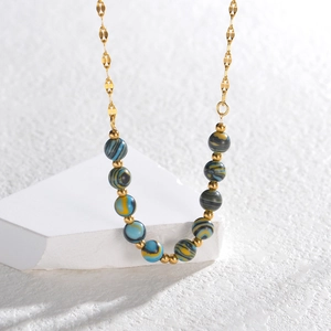 Gold plated stainless steel necklace with blue and yellow marbled beads on white marble