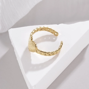 Golden heart ring with hollow chain band texture on a white geometric stone base