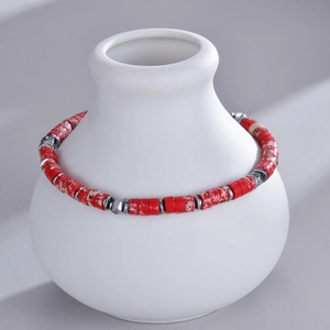 Detail of red marble beads and silver accents on a bracelet around a white vase