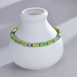 Detailed view of green stone beaded bracelet with silver spacers on a white vase