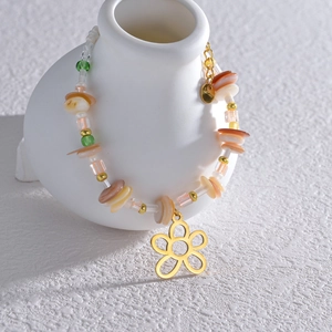 Dettaglio del bracciale di perline con ciondolo a fiore dorato su un vaso di ceramica