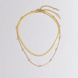Detail of layered gold stainless steel snake chain and beaded necklace with metallic shine