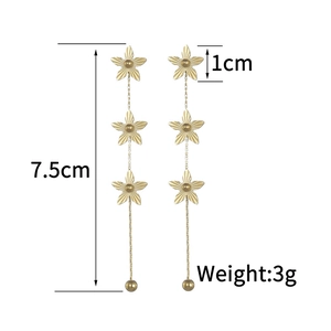 Détail de boucles d'oreilles pendantes dorées avec trois fleurs et pompon de 7,5cm