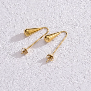 Détail des boucles d'oreilles goutte dorées au fini miroir sur fond blanc texturé