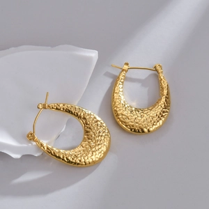 Dettaglio di orecchini a cuore in oro 18K con texture martellata e finitura metallica