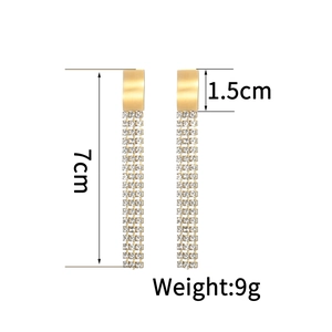 Détail de boucles d'oreilles pendantes dorées de 7cm avec strass blancs et mesures