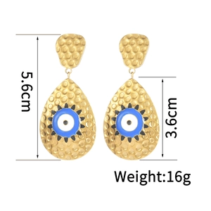 Détail de boucles d'oreilles dorées en goutte avec texture martelée et œil