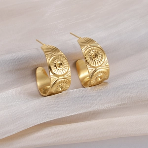 Detail of vintage C-shaped gold earrings with embossed sunburst and geometric textures