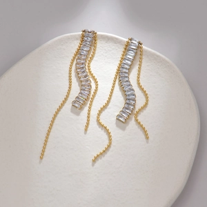 Golden geometric tassel earrings with rectangular zircons on a white ceramic plate